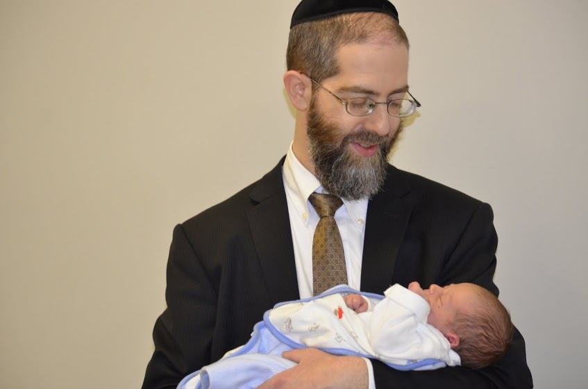 Rabbi Shaoul Hamaoui gently holding a newborn baby